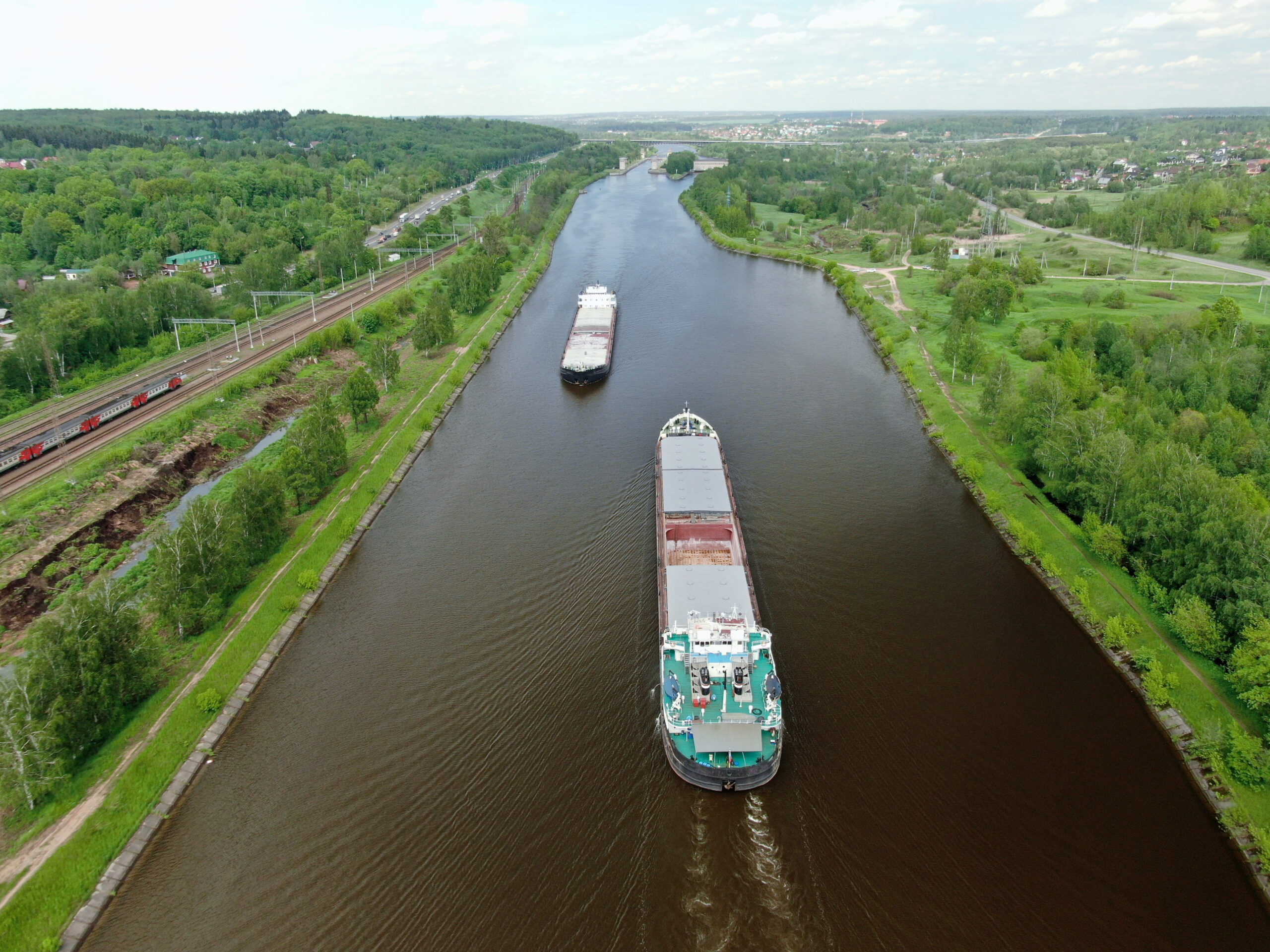 Beautiful panoramic landscape from high altitude two cargo commercial ships sail down the river on counter courses surrounded by green forest in summer with a sunny day